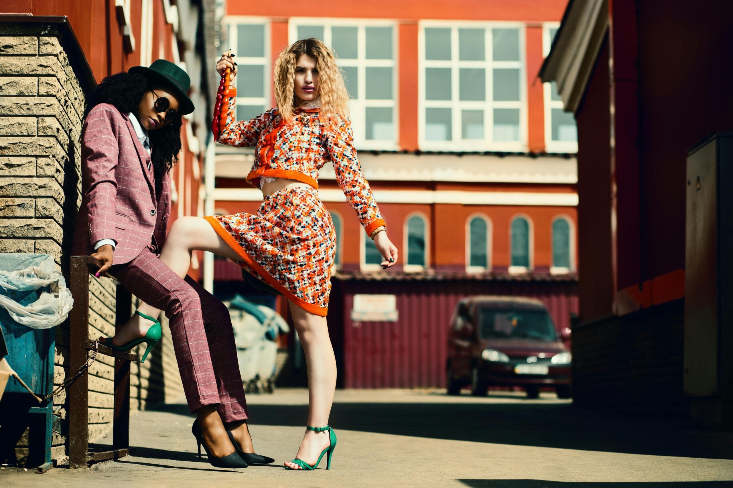 Stylish women posing in an urban alley showcasing contemporary fashion trends.