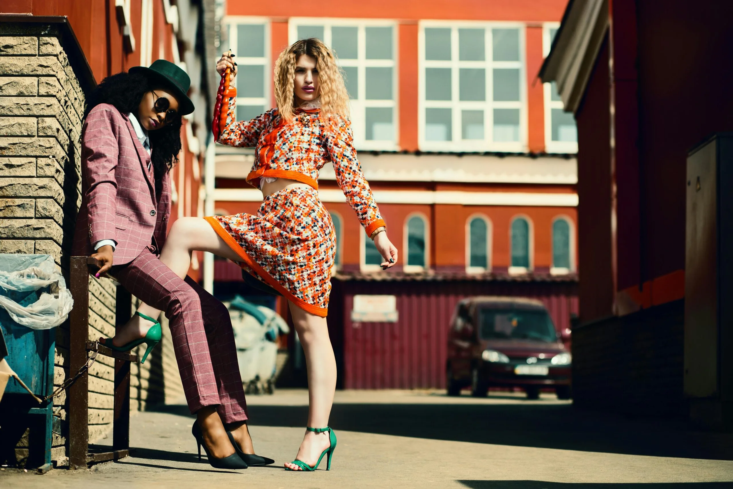 Stylish women posing in an urban alley showcasing contemporary fashion trends.