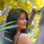 A serene portrait of a woman amidst lush green foliage in daylight.