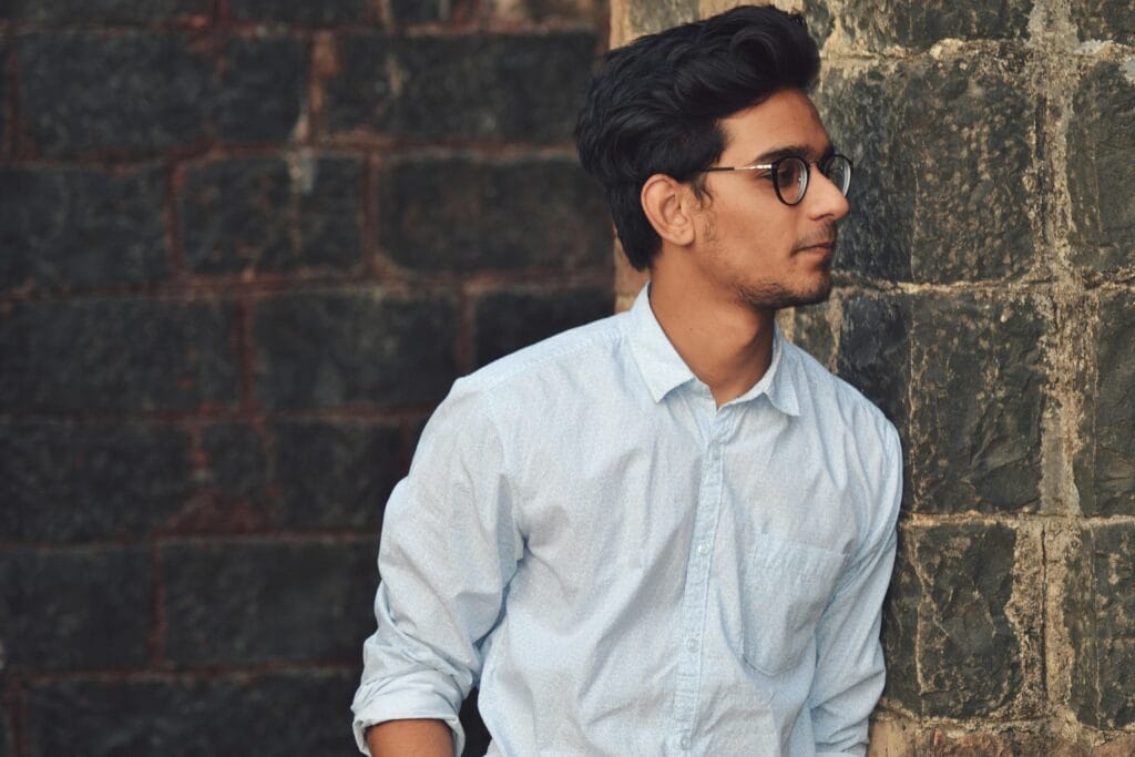 pexels-photo-899357-899357 A stylish young man in glasses leans against a brick wall wearing a casual light blue shirt.